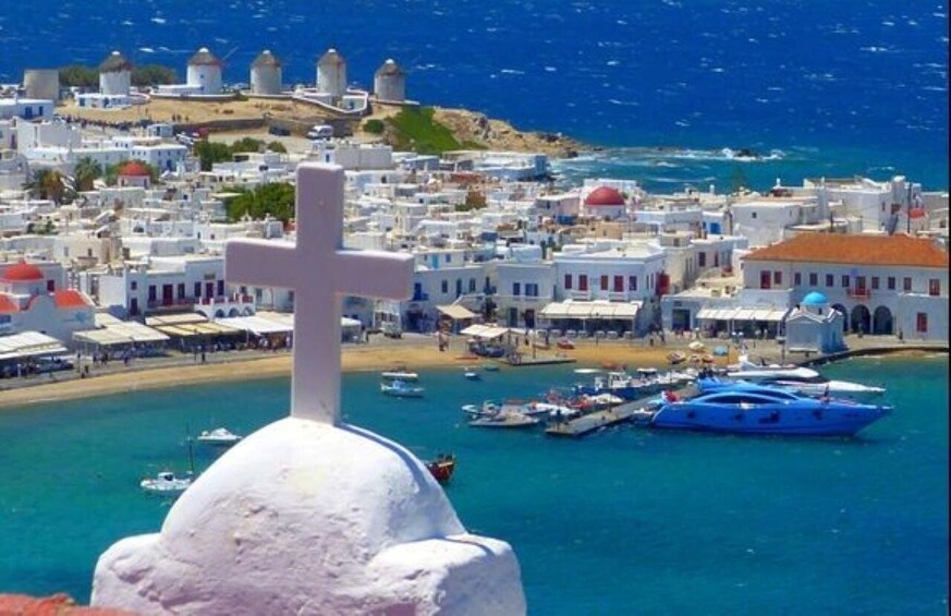 A coastal town with white buildings, a cross, and boats in the harbor. 1
