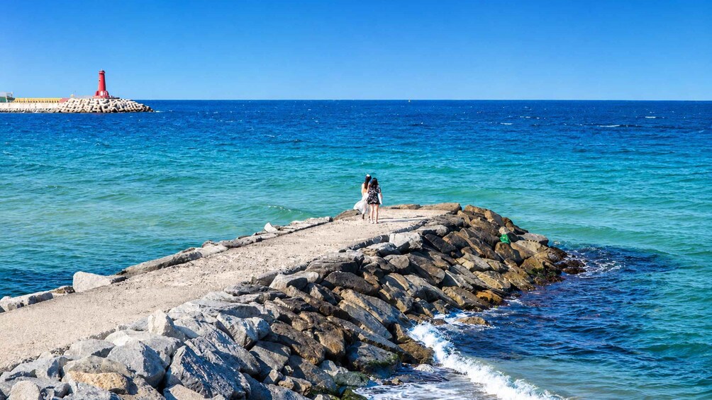A rocky pier extending into the sea with a red lighthouse in the distance. 4
