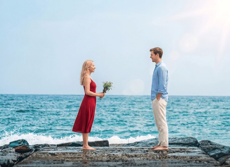 A couple standing on a rocky shore by the sea, with the ocean in the background. 1