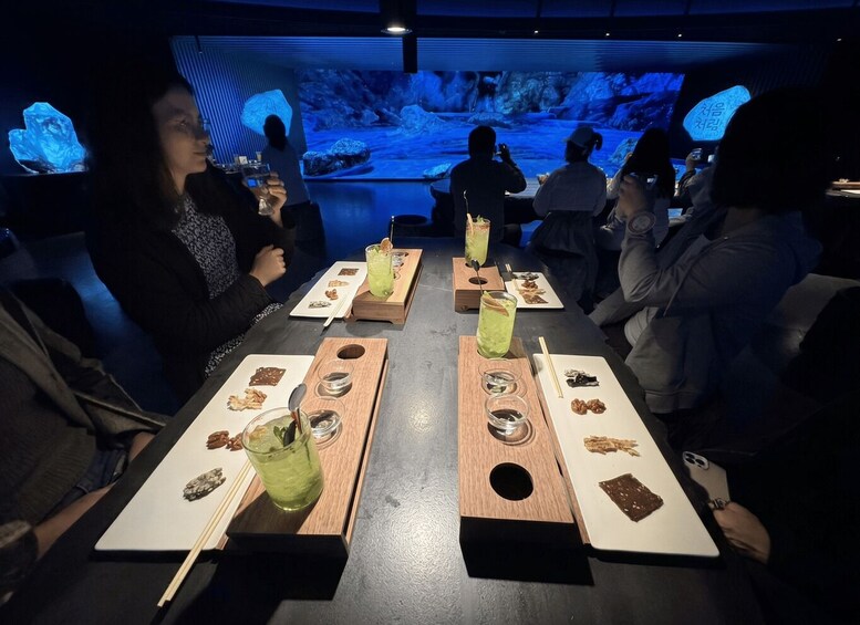 A group of people seated at a table with drinks and snacks, with a large aquarium display in the background. 5