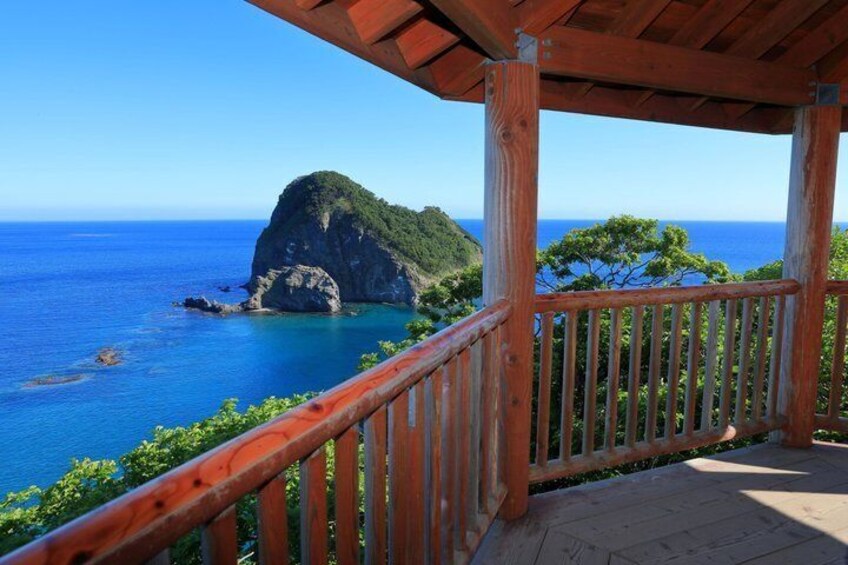 A wooden deck overlooking a coastal view with a prominent green hill and clear blue sea. 1
