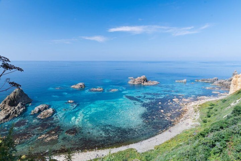A coastal landscape with clear turquoise waters, rocky outcrops, and a grassy hillside. 5