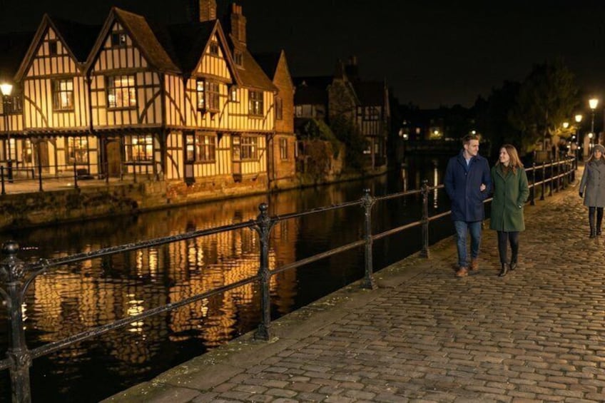 A river with a bridge, a row of illuminated Tudor-style houses, and a cobblestone walkway. 3
