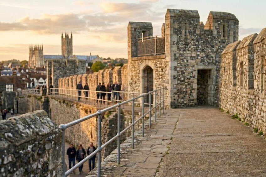 A stone pathway leading to a historic castle wall with a cathedral in the background. 2