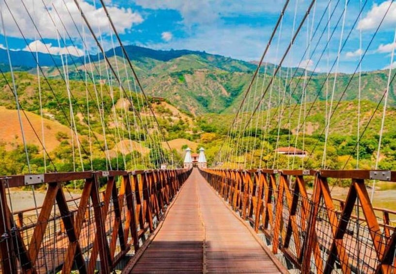 A wooden suspension bridge with metal railings, surrounded by green hills and a clear sky. 1