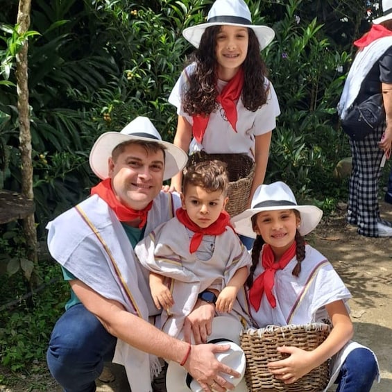 A group of people in outdoor attire, including hats and scarves, gathered in a natural setting with dense foliage. 1