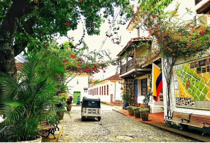 A cobblestone street lined with lush greenery and colorful buildings, a tuk-tuk parked in the middle, and a bench on the right. 5