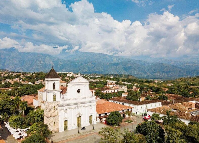 A white church with a bell tower, surrounded by a town with red-roofed buildings and green hills in the background. 3