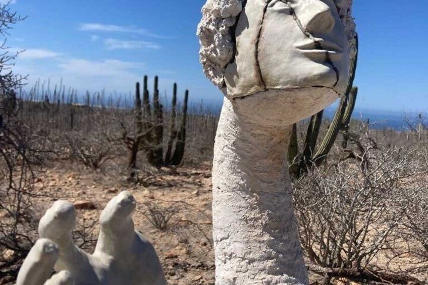 A desert landscape with a large white statue of a human head and hands, surrounded by cacti and sparse vegetation. 4