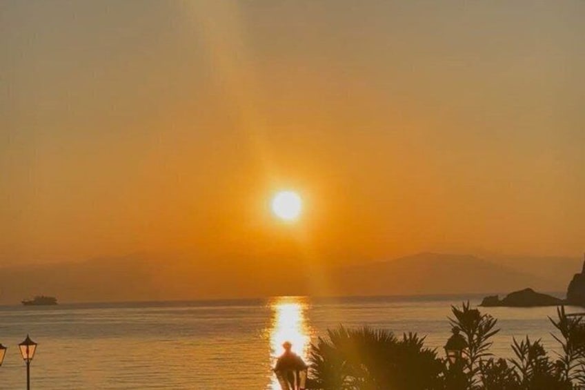 A sunset over a calm sea with a silhouette of a person and distant land. 1