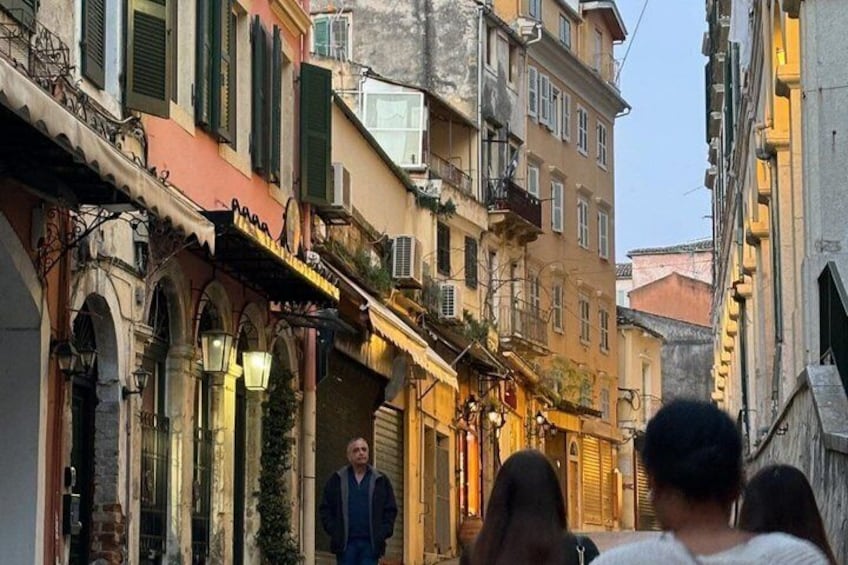 A narrow street with buildings featuring arched doorways and awnings, suggesting a historic European town. 3