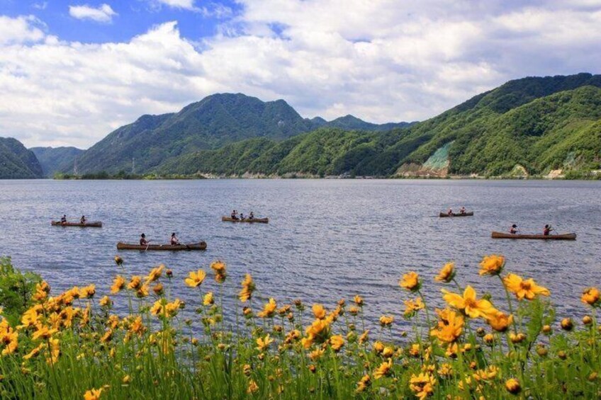 A calm lake with canoes, surrounded by lush green hills and yellow flowers in the foreground. 5