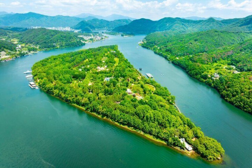 A lush green island surrounded by a river, with mountains in the background. 1