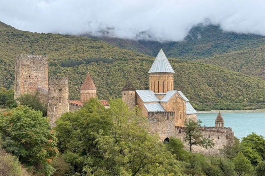 A historic castle with a church, surrounded by lush greenery and a lake. 3