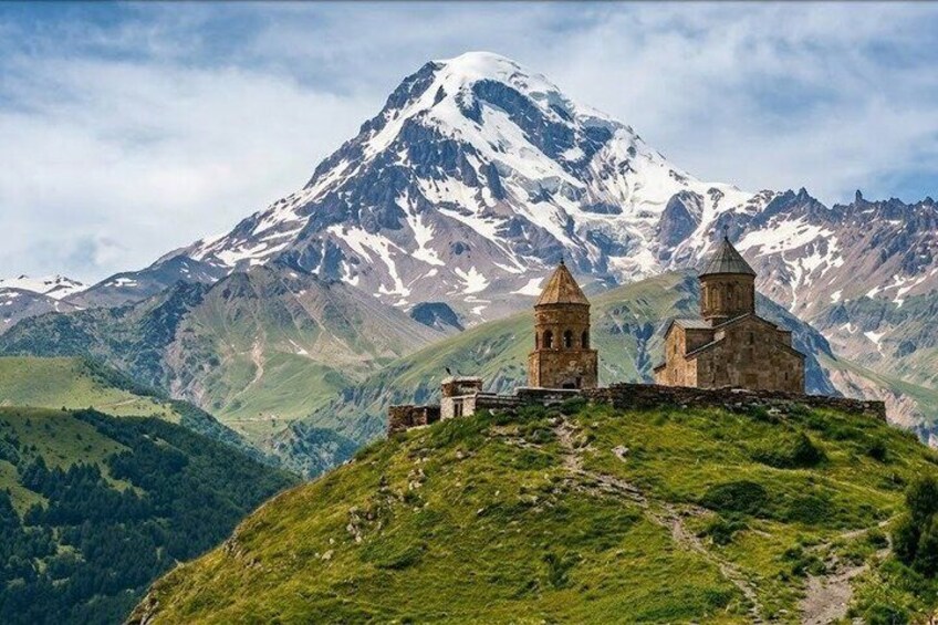 A mountainous landscape with a church on a hill and a snow-capped peak in the background. 1