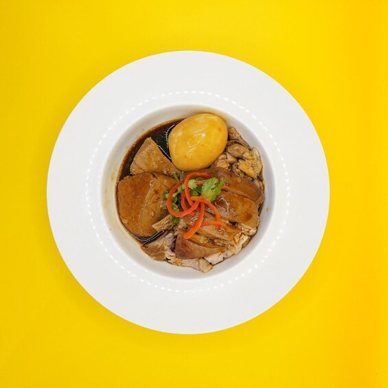 A bowl of soup with meat and vegetables on a white plate against a yellow background. 1
