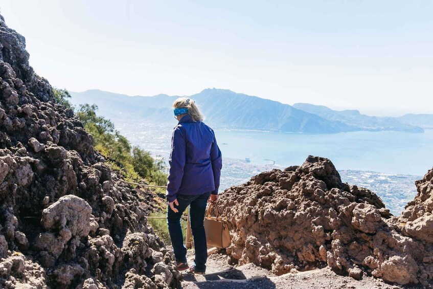 A person standing on rocky terrain overlooking a body of water and distant mountains. 3