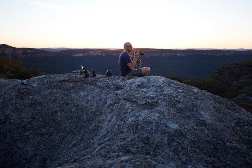 A person sitting on a rock with a camera, overlooking a canyon. 3