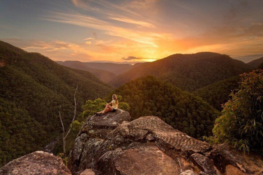 A person sitting on a rock with a sunset in the background. 2