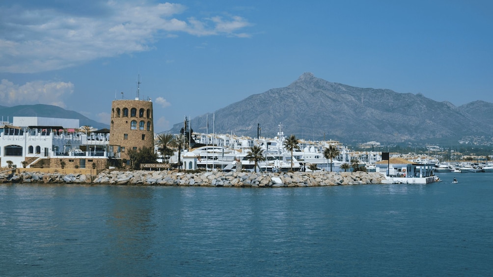 A coastal marina with yachts, a historic tower, and a mountain in the background. 3