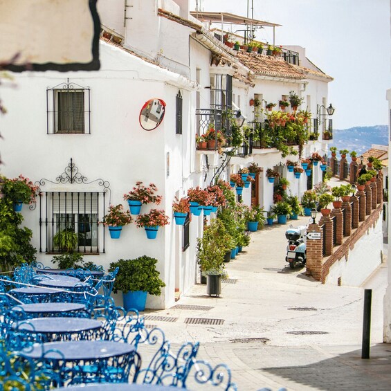 A narrow street with white buildings, blue outdoor furniture, and potted plants. 1