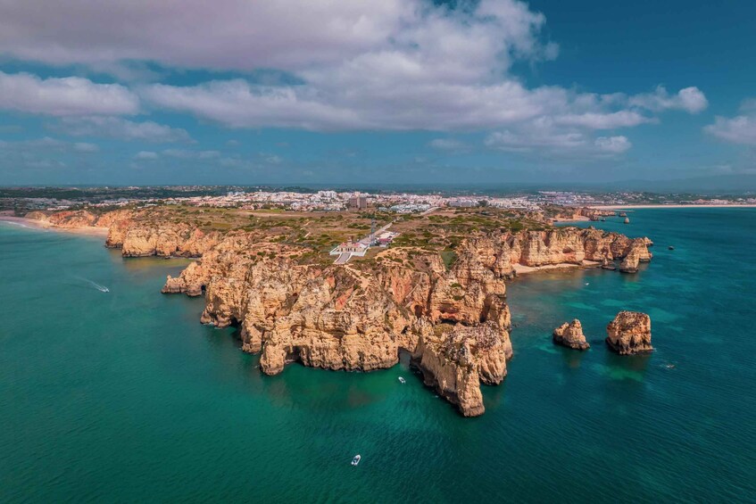 A coastal landscape with rocky formations, clear turquoise waters, and a distant cityscape. 3