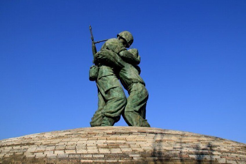 A statue of soldiers on a brick pedestal against a clear blue sky. 3