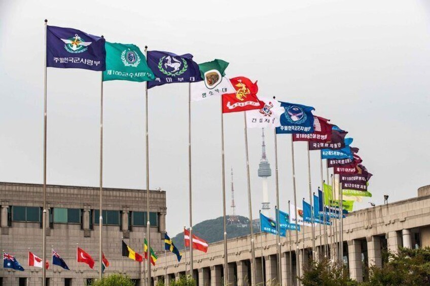 A row of flags on flagpoles in front of a building with a tower in the background. 2