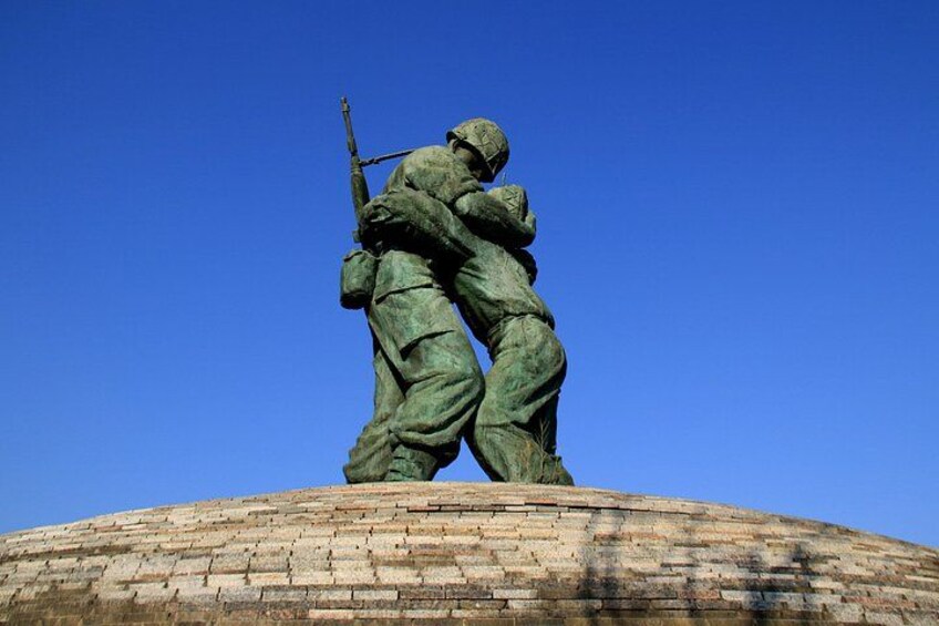 A statue of two soldiers on a brick pedestal against a clear blue sky. 3