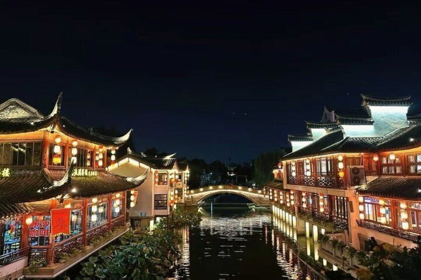 A traditional Chinese water town at night with illuminated buildings and a bridge over the water. 2