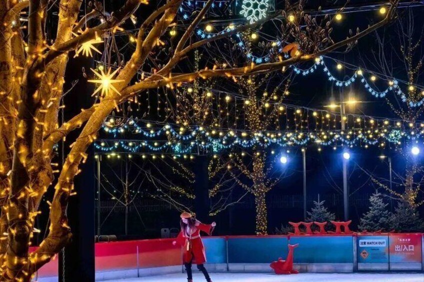 An ice skating rink with overhead string lights and a red sculpture. 4