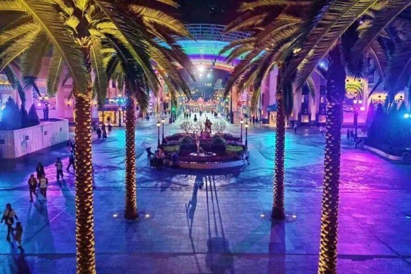 A nighttime scene with palm trees, a fountain, and illuminated structures. 3