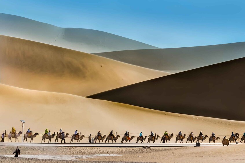 A caravan of camels and riders traversing a desert landscape with undulating sand dunes. 2