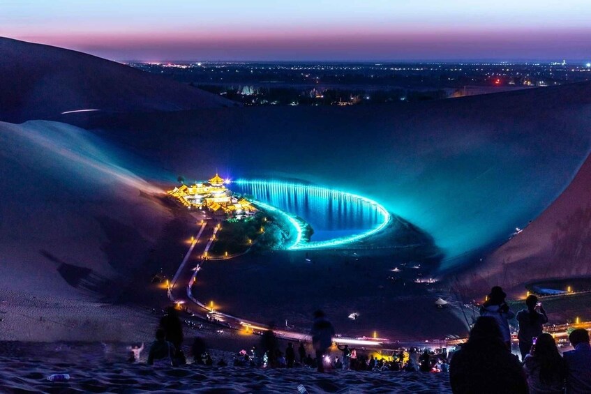 A nighttime desert landscape with a lit fountain and a distant cityscape. 4