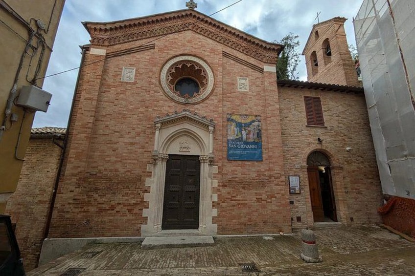 A brick building with a circular window and a door, a bell tower, and a banner. 2