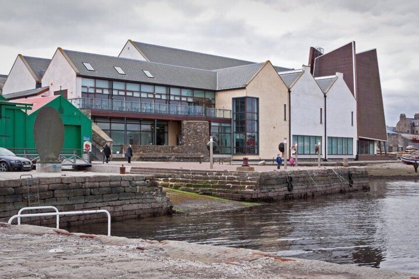 A waterfront with a modern building, a green structure, and a stone wall. 2