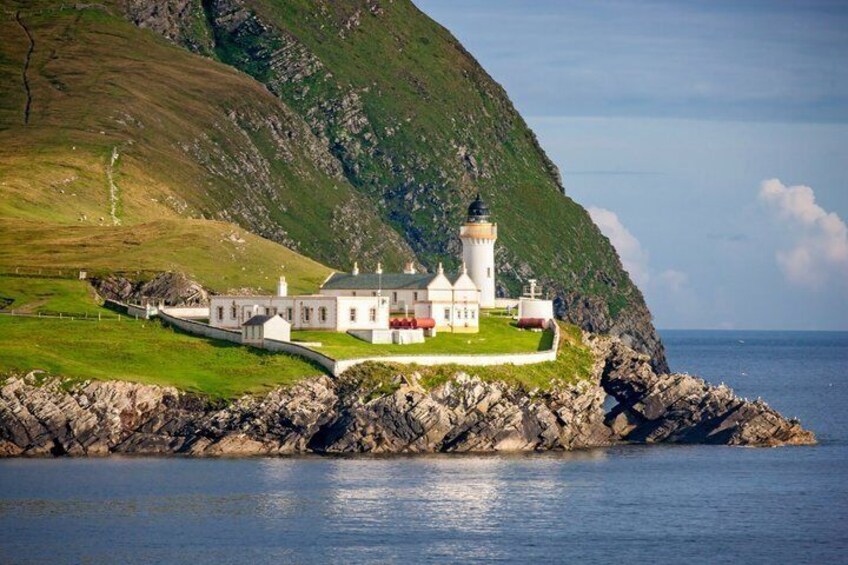 A lighthouse and a white building on a rocky coastline. 1
