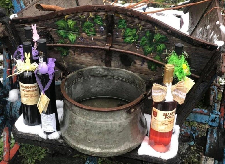 A rustic wooden cart with two bottles of wine and a metal pot. 4