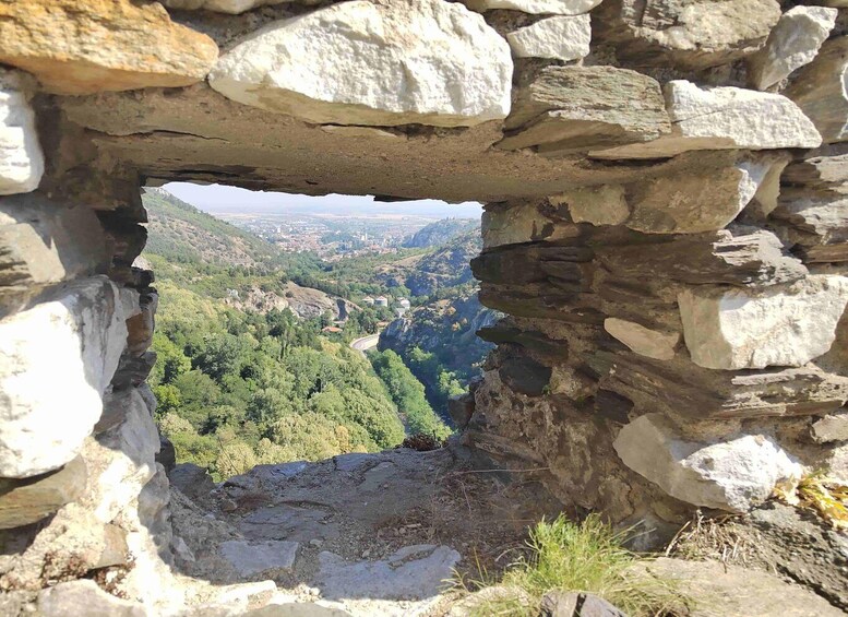A stone archway overlooking a valley with a winding road and scattered buildings. 5