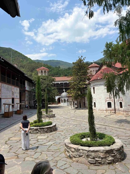 A courtyard with stone paving, a central dome, and surrounding buildings with red-tiled roofs. 2