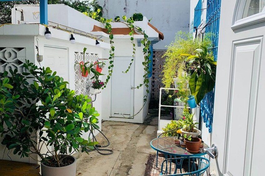 A narrow courtyard with a white door, a blue chair, and potted plants. 2