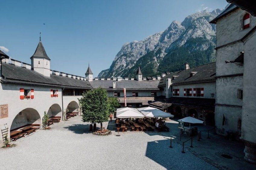 A courtyard with buildings, a tree, and mountains in the background. 3