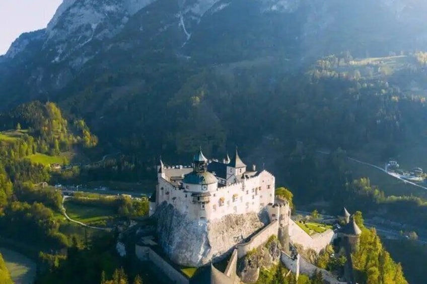 A castle on a hill with a river in the foreground and mountains in the background. 1