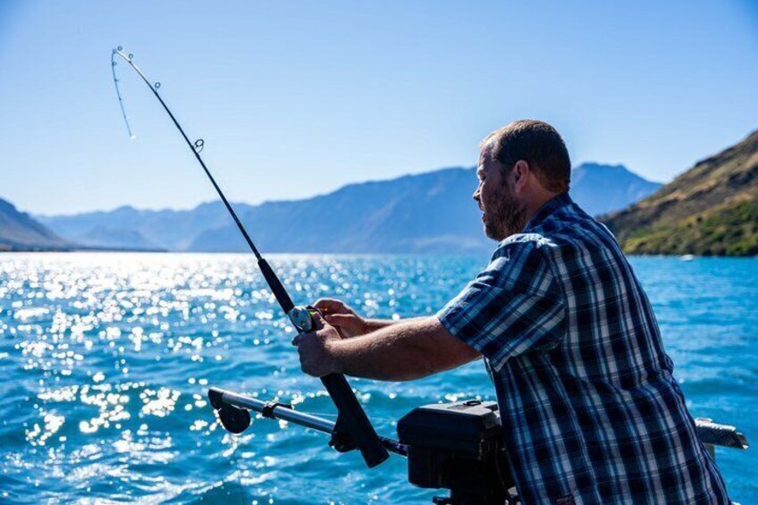 A person fishing by a lake with mountains in the background. 2