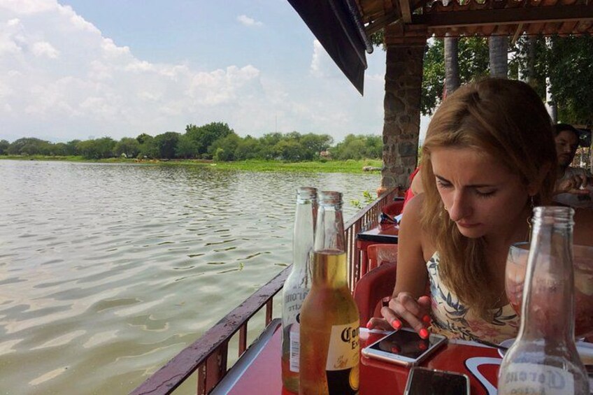 Une personne est assise à une table près d’un bateau et de bouteilles, sur une rivière paisible. 2
