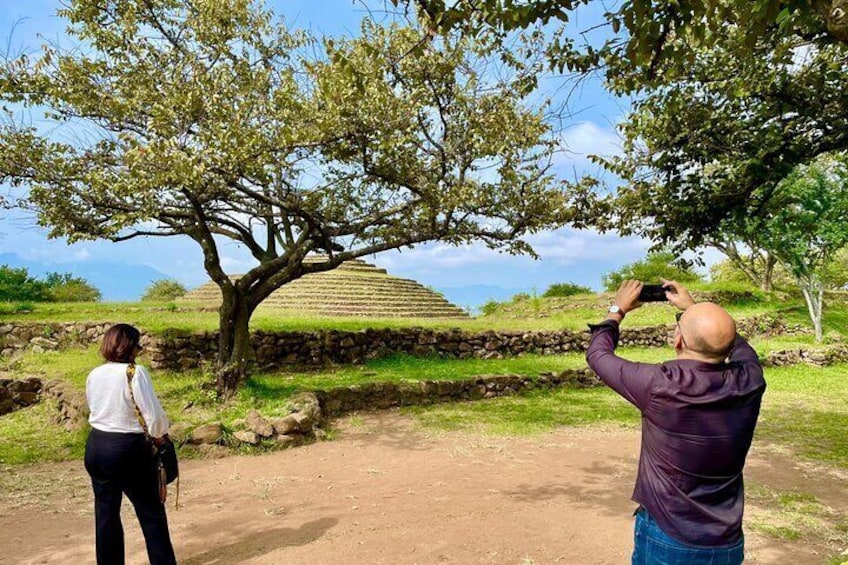 A person taking a photo of a tree with a person standing in the foreground. 1