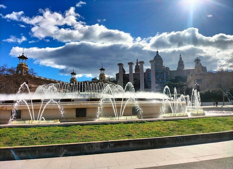 A fountain with water jets in front of a historic building with multiple towers. 1
