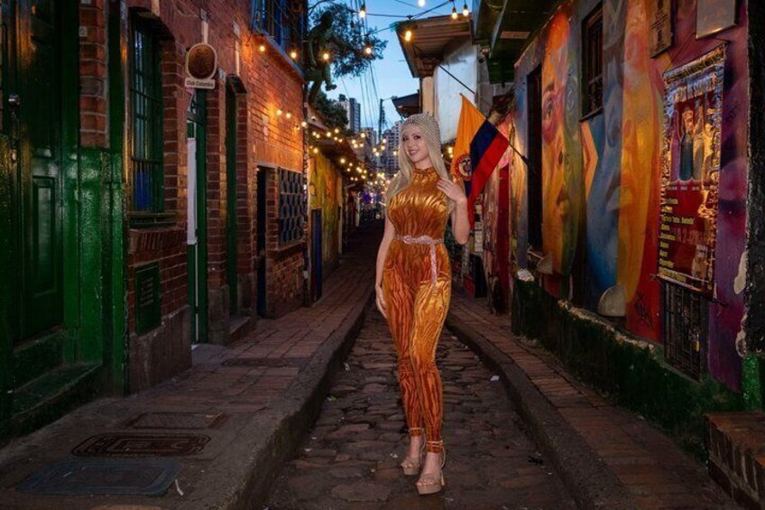 A woman in a golden dress walking down a narrow street lined with colorful buildings and string lights. 4