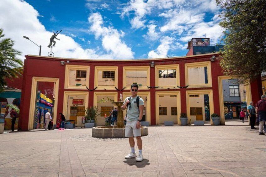 A person standing in front of a red and yellow building with a fountain in the center. 3