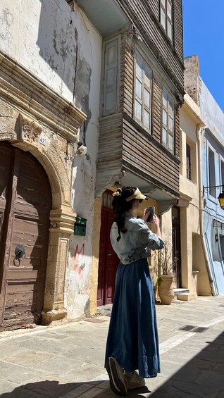 A person taking a photo with a smartphone in front of a historic building with a weathered facade and a red door. 5